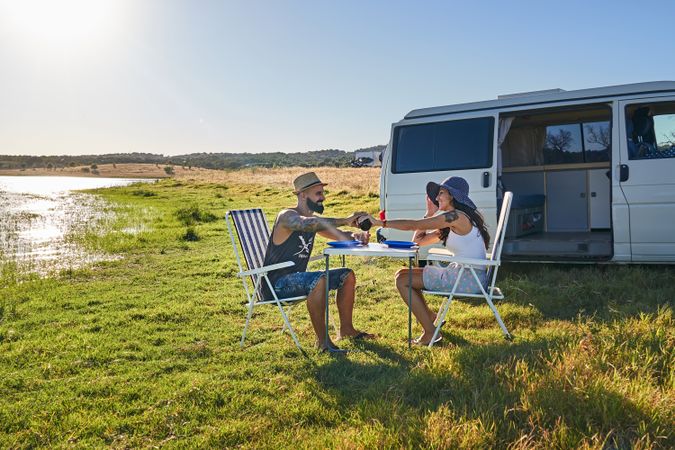 Woman and man sitting on chairs at table on shore near car