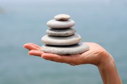 Side view of hand with small pile of rocks with ocean view in background