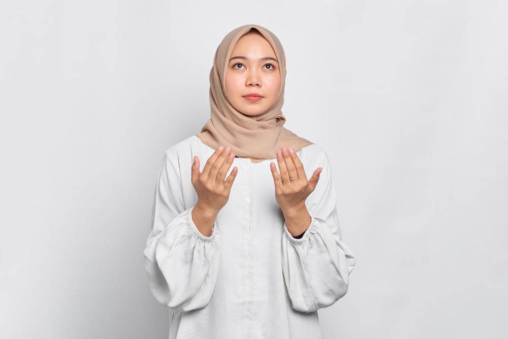 Muslim woman in headscarf and light blouse looking up in prayer