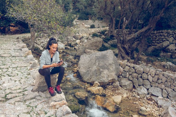 Woman with smartphone resting near fast stream