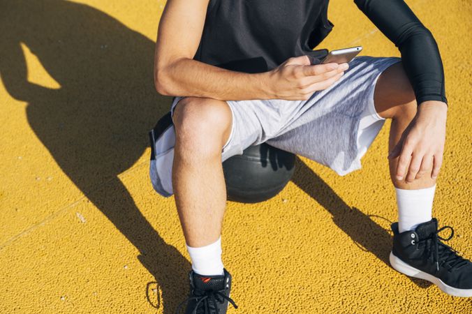 Male basketball player using his smartphone resting after training
