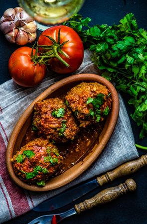 Large meatballs served on table surrounded by fresh vegetables and herbs