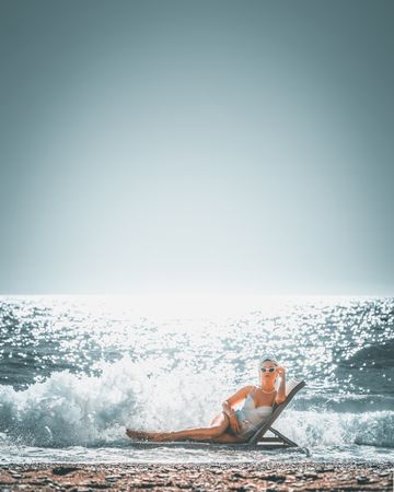 Woman in swimsuit laying on lounge chair on sea wave