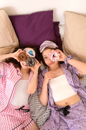Girls in striped pajamas enjoying donuts during playful sleepover.