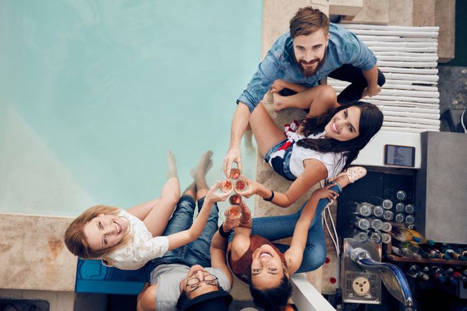 Multiracial young people sitting by the pool having wine during party