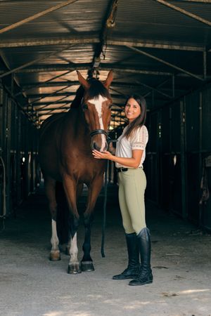 Cheerful equestrian with horse in stall