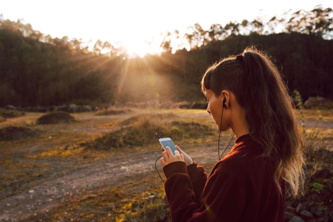 Young woman with piercing listening music on smartphone on hill