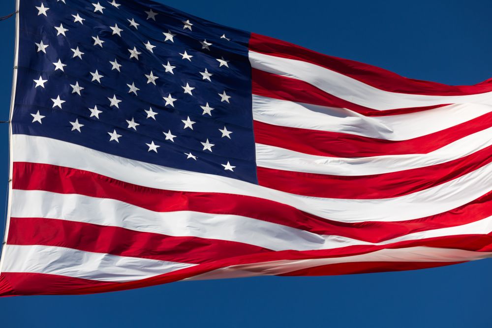 American Flag Waving In The Wind Against Deep Blue Sky.
