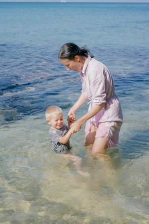 Woman and small kid having fun with water while relaxing on seacoast at resort