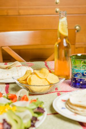 Traditional mexican food with a bowl of nachos, a plate of chicken fajita, tortillas, fresh salad and a fresh beer