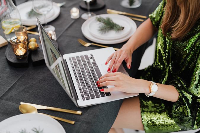Cropped image of woman in green dress using computer sitting at a dinner table