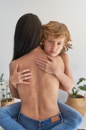 Boy hugging faceless topless mother