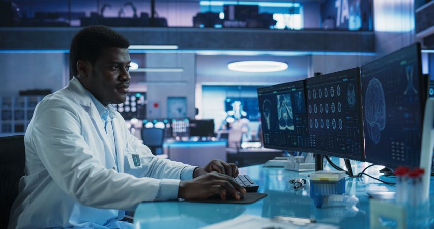 Black Male Neuroscientist Using Desktop Computer To Analyze MRI Scans Of Brain In Medical Research Center Lab.