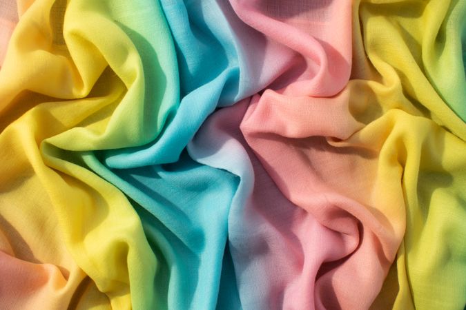 Gradient yellow blue pink and green fabric wavy crumpled background texture.