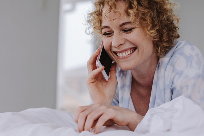 Close up of a smiling woman talking over mobile phone lying on bed