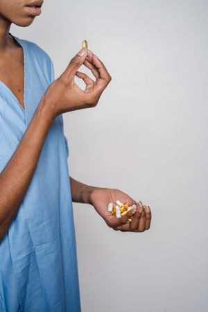 Cropped image of Black woman taking medicine against light background