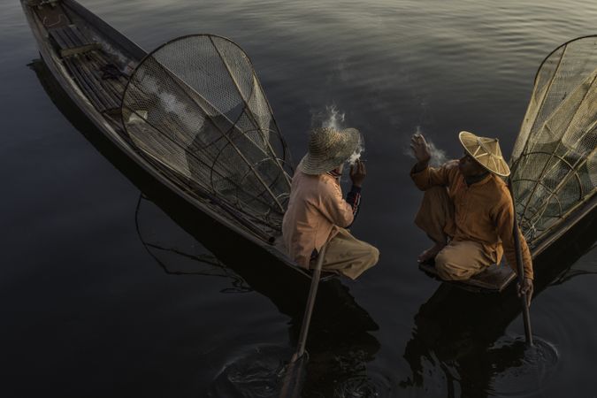 Two Asian fisherman smoking and sitting on boats in Myanmar