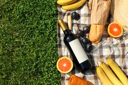 Bottle of wine, baguette, fruits, straw hat and towel on grass, space for text