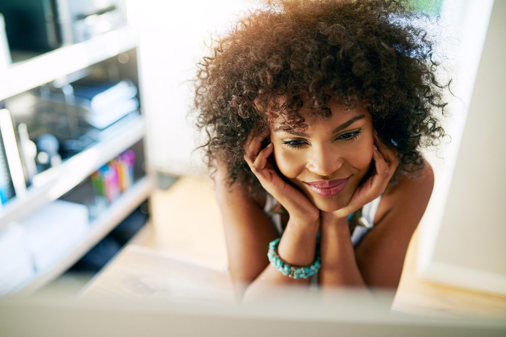 Female with curly hair resting her chin in her hands in front of her work computer