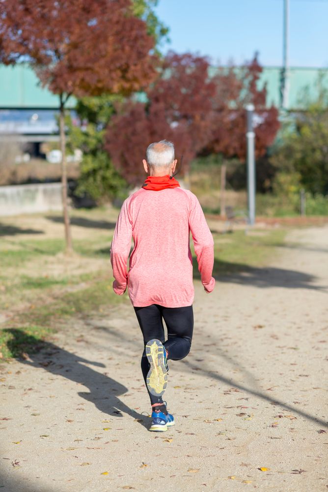 Back of mature man in red shirt jogging outside in park