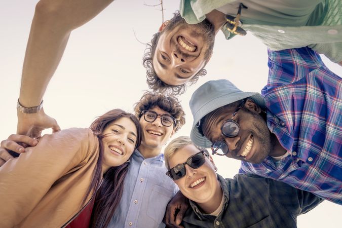 Low angle point of view shot of happy diverse friends in a huddle outdoors.