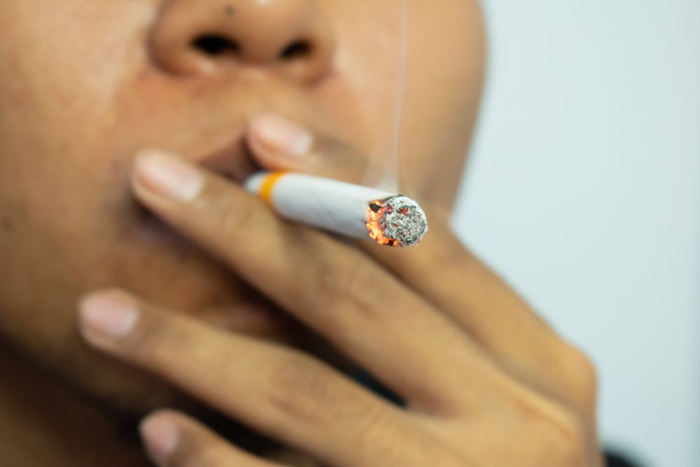 Unrecognizable person holding a lit cigarette to their mouth