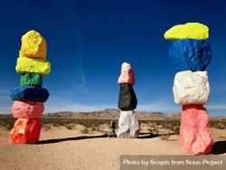 Person standing beside stacks of colorful rocks in desert 4AoOE0