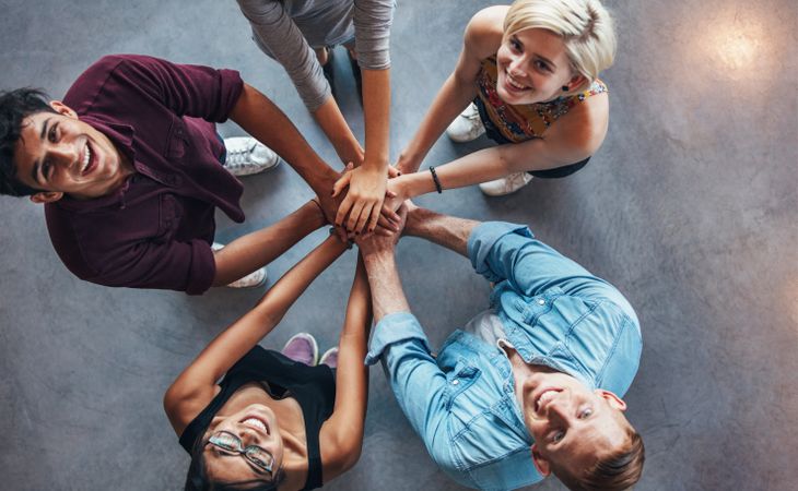Overhead view of young people standing together looking up at camera with hands together