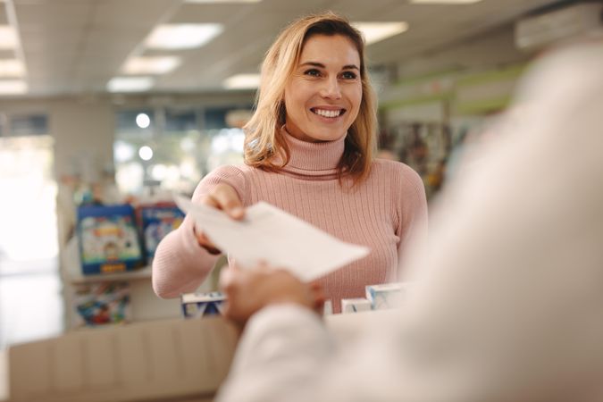 Woman standing at medical store counter and handing a prescription to pharmacist