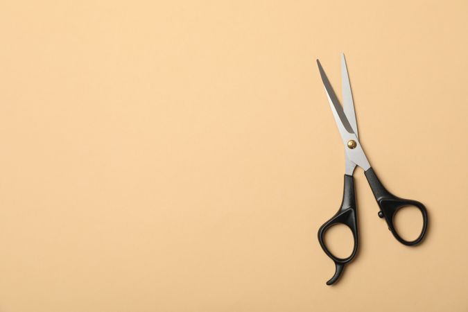 hairdresser scissors on beige background, space for text