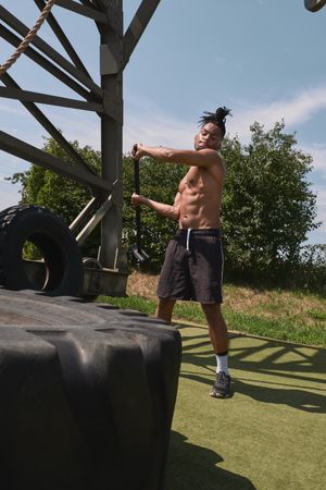 Muscular Black guy hammering tire in outdoor gym