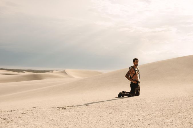 Man kneeling on sand dune and looking away