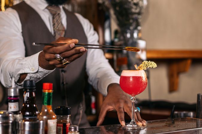 Close-up of an unrecognizable Black bartender pouring a cocktail and decorating it with garnish