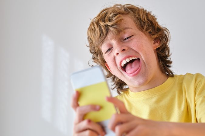 Happy boy taking selfie on smartphone on light background
