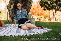 Young woman reading a book sitting on a blanket at the park 0vrEZ0