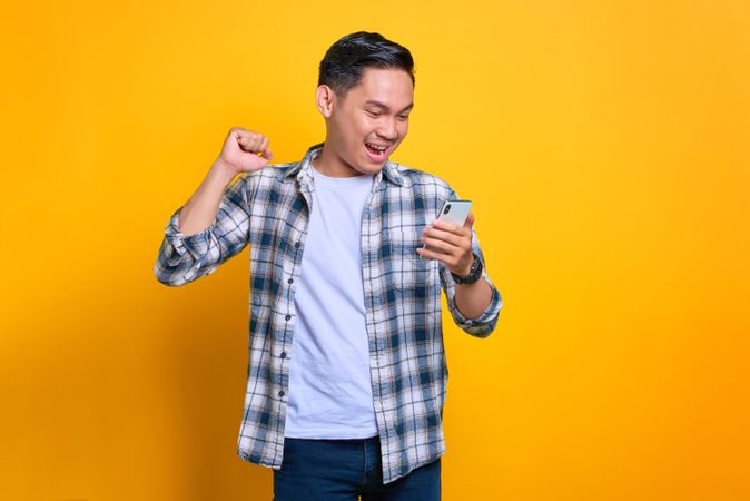 Asian male receiving good news looking down at his phone in studio shoot