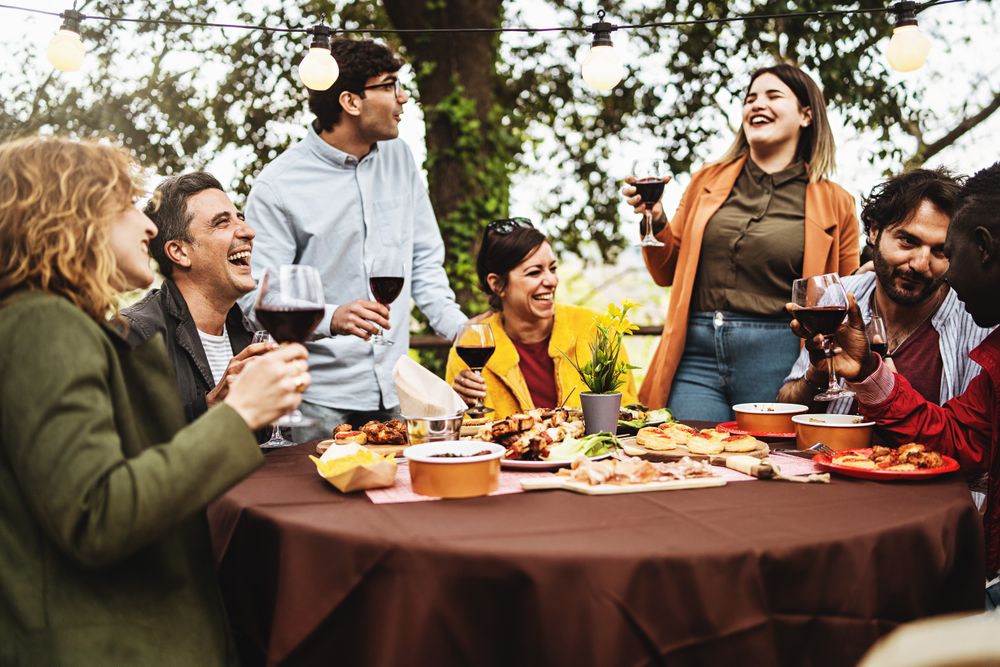 Group of multi-ethnic carefree friends talk, joke and drink wine during the brunch of a harvest wine tasting