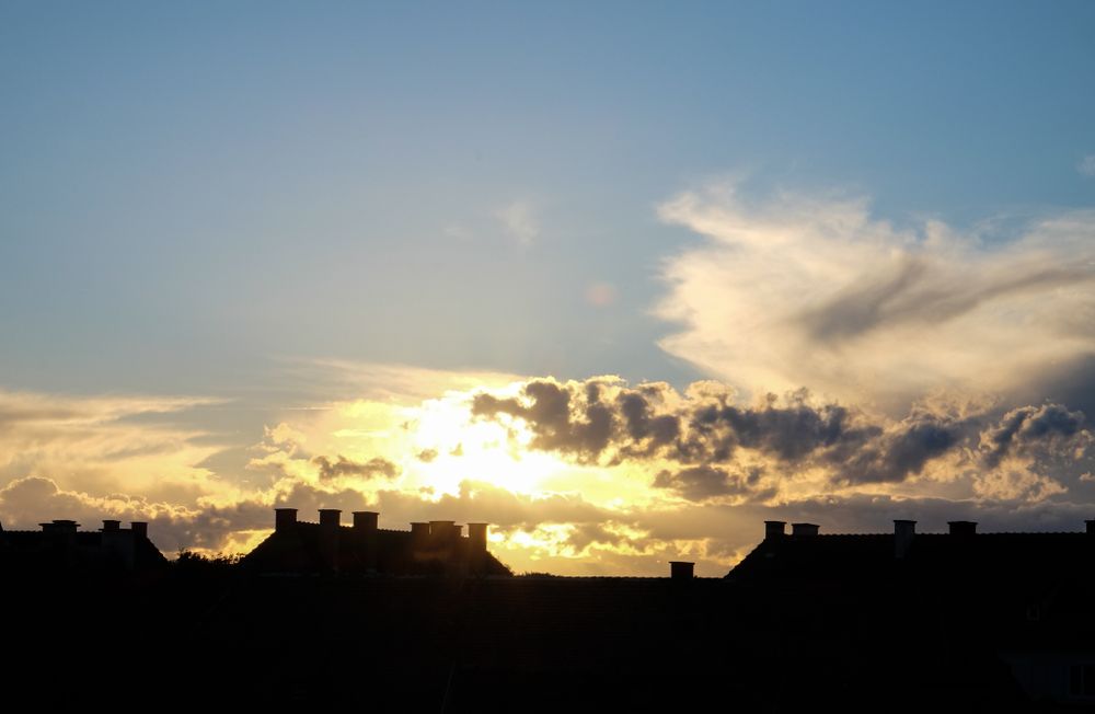 Blue sky with fluffy clouds over houses in the shadows