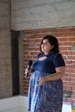 Woman holding a microphone giving a talk with an exposed brick wall behind her