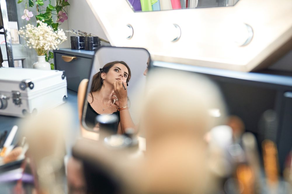 Faceless master painting lips of woman reflecting in mirror