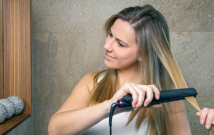 Smiling young woman straightening hair with a straightener