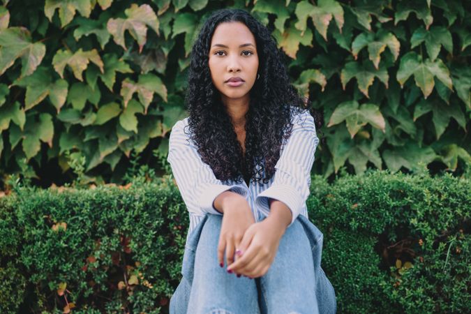 A contemplative young woman sits peacefully in lush greenery, embodying elegance and calm