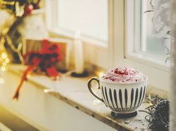 Mug with hot chocolate and whipped cream on window sill with candle, present and warm light
