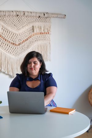 Woman sitting with laptop with macramé on wall