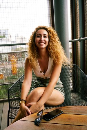 Smiling woman sitting in designed metal chair with sunglasses in hand
