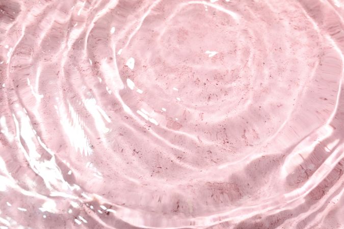 Top view of clear water with ripples in pink background with copy space