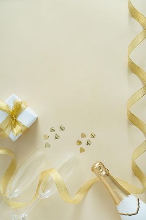 Present wrapped with gold ribbon, champagne bottle, and champagne flutes with heart glitter
