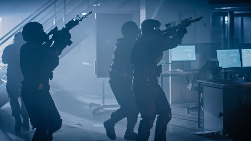 Shot of Masked Squad of Armed SWAT Police Officers Storm a Dark Seized Office Building with Desks and Computers.