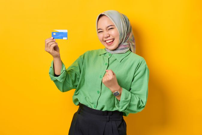 Muslim woman in headscarf and green blouse holding gift card she won