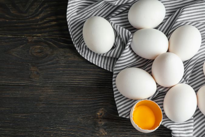 Chicken eggs in kitchen towel on wooden background, space for text